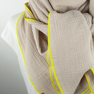 Puede incluir: Una bufanda de algod&oacute;n beige con ribete amarillo. La bufanda est&aacute; doblada y drapeada alrededor del cuello de una persona. El nombre de la marca "wundabar" es visible en la bufanda.