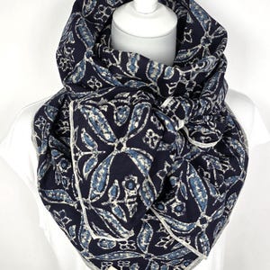 May include: A navy blue and white patterned infinity scarf. The scarf features a repeating floral design in shades of blue and white. The scarf is wrapped around a white mannequin head and shoulders.