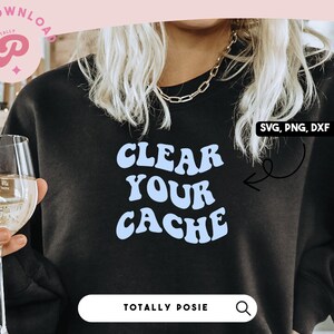 以下が含まれることがあります： 青いレトロな文字で「CLEAR YOUR CACHE」と書かれた黒いスウェットシャツ。スウェットシャツは、白ワインのグラスを持った人が着用しています。画像の右上隅には「SVG、PNG、DXF」というテキストが表示されています。
