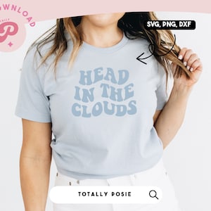 May include: A light blue t-shirt with the text "Head in the Clouds" in a retro font. The text is in a light blue color. The t-shirt is being worn by a person.