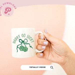 Puede incluir: Taza de cer&aacute;mica blanca con un dise&ntilde;o verde que dice "Happy Go Lucky" con dos dados verdes colgando de una cinta verde.