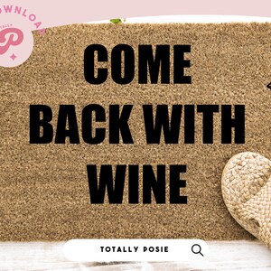 Op de afbeelding: Een bruine deurmat met de tekst "Come Back With Wine" in zwarte letters. De deurmat ligt op een wit houten oppervlak met groene klimop planten aan de linkerkant. Twee strooien sandalen liggen aan de rechterkant van de deurmat.