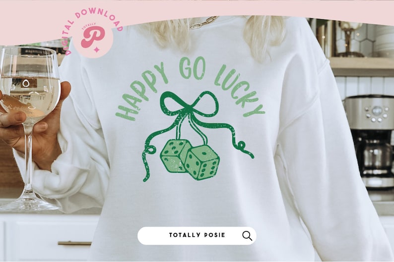Puede incluir: Sudadera blanca con texto verde que dice "Happy Go Lucky" con un lazo verde y dos dados colgando del lazo.