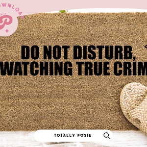 May include: A brown doormat with the text "DO NOT DISTURB, WATCHING TRUE CRIME" in black lettering. The doormat is on a white wooden surface with green ivy.