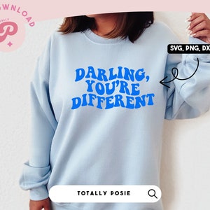 May include: A light blue sweatshirt with the text "Darling, You're Different" in blue, retro-style lettering. The text is centred on the front of the sweatshirt.