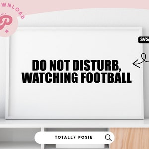 Peut inclure: Une impression encadrée blanche avec du texte noir qui dit "NE PAS DÉRANGER, REGARDER LE FOOTBALL". L'impression est sur une étagère blanche avec une tasse blanche et des livres.