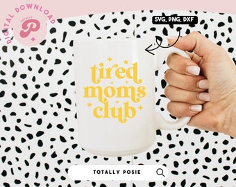 May include: White ceramic mug with a yellow design that says "tired moms club" with stars. The mug is being held by a hand.