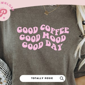 Puede incluir: Una camiseta gris con el texto "GOOD COFFEE GOOD MOOD GOOD DAY" en letras rosas de estilo retro. El texto está centrado en la camiseta.