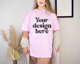 Pode incluir: Camiseta rosa claro com o texto "Your design here" em fonte preta desgastada. A camiseta é usada com um envoltório de malha bege. A imagem é uma maquete de produto, ideal para mostrar designs de camisetas personalizados.