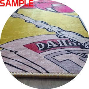 Puede incluir: Una alfombra circular con un dise&ntilde;o de dibujos animados. La alfombra presenta un fondo amarillo con una ilustraci&oacute;n de estilo c&oacute;mic. La palabra "DAILY" es visible en un elemento similar a un peri&oacute;dico. La alfombra tiene un borde marr&oacute;n.