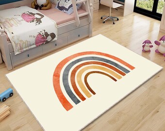 May include: A white rug with a large, colorful rainbow design. The rainbow has six bands of color: orange, red, brown, yellow, gray, and blue. The rug is on a wooden floor.
