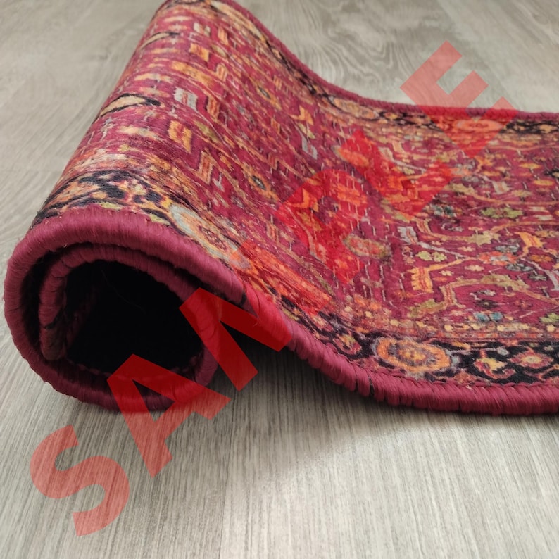 Pu&ograve; includere: Un tappeto da corridore arrotolato con un motivo rosso, arancione e nero e un bordo marrone scuro. Il tappeto &egrave; arrotolato e il bordo del tappeto &egrave; visibile.