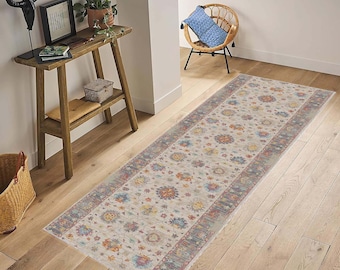 May include: A long, rectangular, cream-colored rug with a floral pattern in shades of blue, red, and yellow. The rug has a border with a geometric pattern in shades of blue, red, and brown. The rug is laid out on a wooden floor.