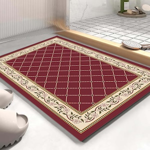 Può includere: Un tappetino da bagno rettangolare con un centro bordeaux intenso e un motivo a griglia a rombi bianchi. Il bordo è color crema e decorato con un motivo ripetuto di tralci floreali nei toni del verde, marrone e rosa tenue.