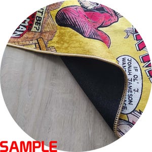 Puede incluir: Alfombra redonda amarilla con un dise&ntilde;o de c&oacute;mic que presenta a Spider-Man. La alfombra tiene un reverso negro y un borde beige. El texto "MAN" y "T BE?" son visibles.