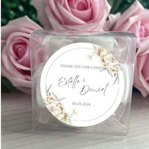 May include: A white round favor tag with a floral design and the text "Thank you for coming Estelle & Daniel 02.25.2024".
