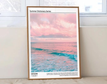 May include: A framed print with a pink and blue sunset over the ocean. The text on the print reads "Summer Dictionary Series" and "OCEAN /'oʊʃən/  A large body of saltwater that has high waves and powerful winds, waves with its waves, a peaceful place where your spirit finds serenity, and a source of inspiration to live wild and free."