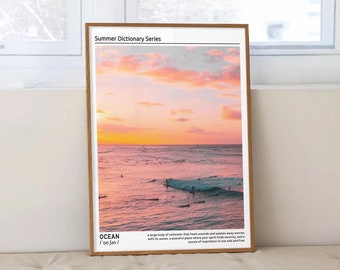 May include: A framed print with a pink and orange sunset over the ocean. The print has the text "Summer Dictionary Series" and "OCEAN /ˈoʊ.ʃən/" with a definition of the word ocean.