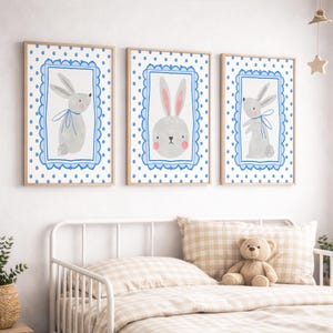 May include: Three framed watercolour prints of cute grey rabbits. Each print has a blue scalloped border and a white background with blue polka dots. The rabbits have pink accents and blue bows.