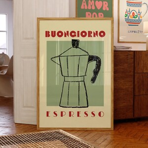 Könnte beinhalten: Ein gerahmter Kunstdruck mit einer Kaffeemaschinen-Illustration und den roten Worten "BUONGIORNO ESPRESSO". Zwei weitere gerahmte Drucke sind sichtbar, einer mit den Worten "MORE AMOR POP" und ein weiterer mit einem Kaffeetassen-Design und den Worten "BUT FIRST, CAFECITO".
