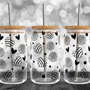 Puede incluir: Tres vasos de vidrio transparentes con diseños de patrones en blanco y negro de corazones y remolinos. Cada vaso tiene una tapa de madera y una pajita de metal.