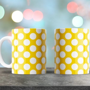 May include: Two white ceramic mugs with yellow polka dot patterns. The mugs are on a gray surface.