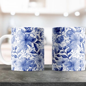 May include: Two white ceramic mugs with a blue floral pattern. The mugs have a white handle and are sitting on a gray countertop.