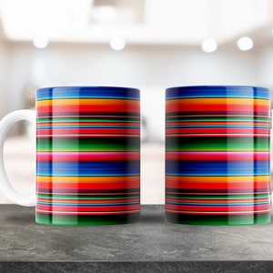 Könnte beinhalten: Zwei weiße Keramikbecher mit einem bunten Streifenmuster. Die Streifen sind rot, orange, gelb, grün, blau und pink. Die Becher stehen auf einer grauen Arbeitsplatte.