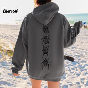 May include: Charcoal-colored hoodie with a drawstring hood and long sleeves. The back of the hoodie features a vertical line of four black insect illustrations. The word "Charcoal" is printed in a cursive font in the upper left corner.