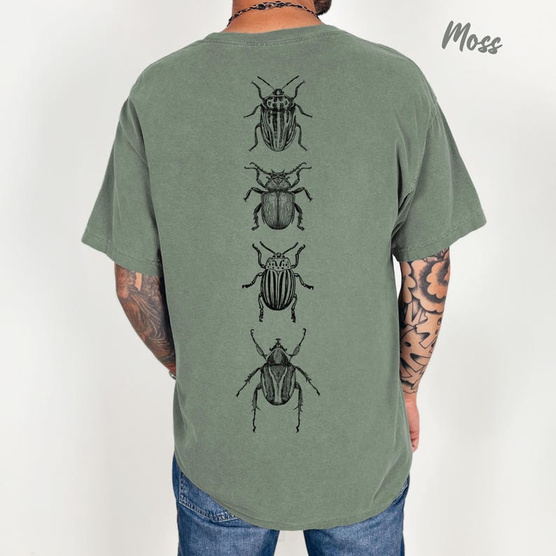 K&ouml;nnte beinhalten: Ein moosgr&uuml;nes Kurzarm-T-Shirt mit einem vertikalen Grafikdruck von vier verschiedenen schwarzen K&auml;fer-Illustrationen in Linienkunst, die mittig auf dem R&uuml;cken platziert sind. Das Shirt hat einen Rundhalsausschnitt und eine lockere Passform.