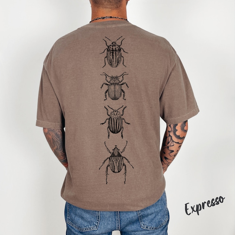 K&ouml;nnte beinhalten: Ein braunes T-Shirt mit kurzen &Auml;rmeln und einem vertikalen Grafikdruck von vier verschiedenen schwarzen K&auml;ferillustrationen auf der R&uuml;ckseite. Das T-Shirt wird mit einer blauen Jeans kombiniert. Das Wort Expresso ist unten rechts schwarz gedruckt.