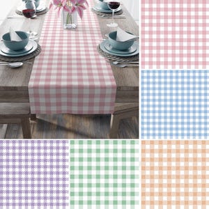 May include: A pink and white checkered table runner displayed on a wooden table, set for a meal. The table is set with plates, bowls, silverware, and wine glasses. A vase of pink flowers is in the center. Additional fabric swatches in pink, blue, purple, green, and orange.