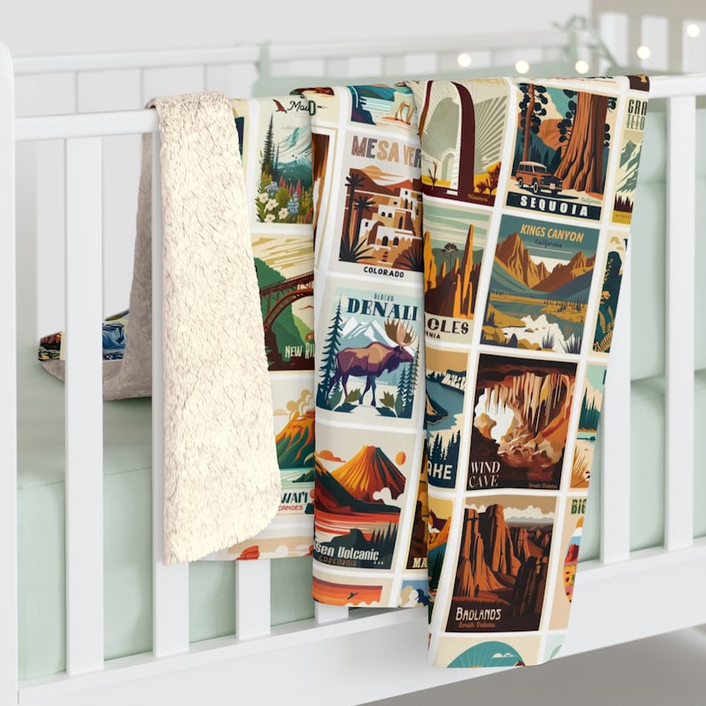 May include: A soft, cream-colored blanket with a collage of vintage travel-themed illustrations. The blanket features images of national parks, including Denali, Sequoia, and Badlands. The blanket is draped over a white crib rail.