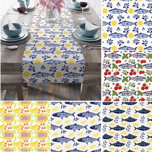 May include: A rectangular table runner featuring a repeating pattern of blue fish, yellow lemon slices, and dark green olive branches on a white background. The design is displayed in various color combinations including red tomatoes and green herbs.