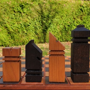 May include: A set of wooden chess pieces in black and brown, arranged on a chessboard. The pieces are stylized and have a modern design.