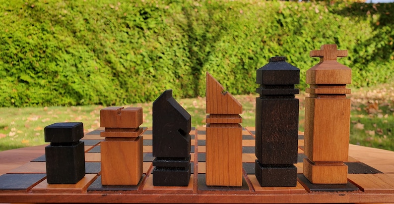 May include: A set of wooden chess pieces in black and brown, arranged on a chessboard. The pieces are stylized and have a modern design.