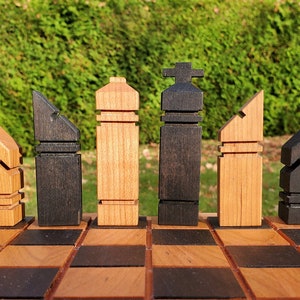 May include: A set of wooden chess pieces in a modern, abstract style. The pieces are arranged on a wooden chessboard with alternating light and dark squares. The pieces are made of light and dark wood, with the light pieces being a natural wood color and the dark pieces being a dark brown color.