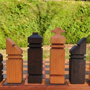 May include: A set of wooden chess pieces in black and natural wood tones. The pieces are arranged in a row on a wooden board. The pieces are stylized and abstract in design.