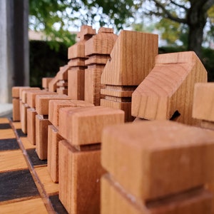 May include: A close-up of a wooden chess set with the pieces arranged on a wooden chessboard. The pieces are made of light brown wood and have a unique, modern design.