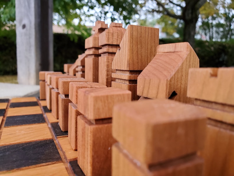 May include: A close-up of a wooden chess set with the pieces arranged on a wooden chessboard. The pieces are made of light brown wood and have a unique, modern design.