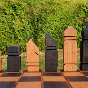 May include: A set of wooden chess pieces in black and brown on a chessboard. The pieces are stylized and have unique designs.