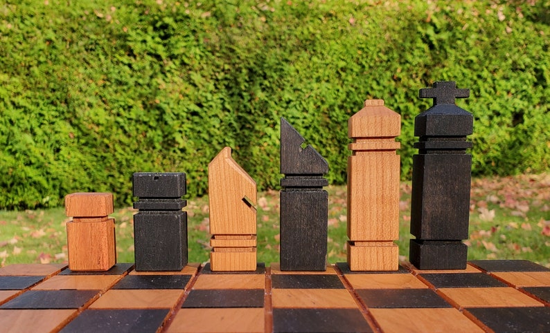 May include: A set of wooden chess pieces in black and brown on a chessboard. The pieces are stylized and have unique designs.