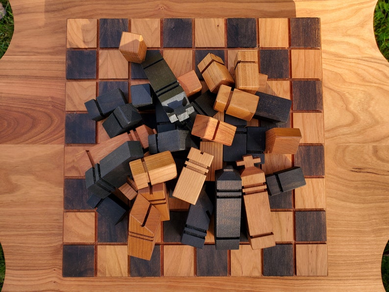 May include: A wooden chessboard with black and brown squares. The board is covered with wooden chess pieces in black and natural wood colors. The pieces are arranged in a random order.