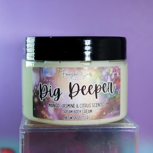 May include: A round plastic jar with a black lid containing body cream. The label features the text "Fairytale Suds", "Dig Deeper", "Mango, Jasmine & Citrus Scented", "Dream Body Cream", and "Net Wt 4oz (113 g)" over a colorful, nebula-like background.