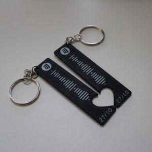 May include: Two black keychains with a Spotify logo and a heart-shaped cutout. Each keychain has a barcode-like design and the text "27/10" on the bottom.