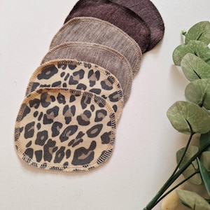 Könnte beinhalten: Ein Stapel wiederverwendbarer Abschminkpads in verschiedenen Braun- und Beigetönen. Die Pads sind aus Stoff und haben einen genähten Rand. Ein Set hat ein Leopardenmuster.