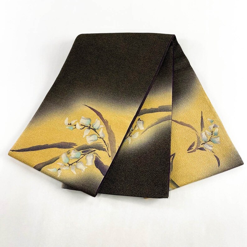 May include: A folded piece of fabric with a brown and gold ombre design. The fabric has a floral pattern with white flowers and dark purple stems.