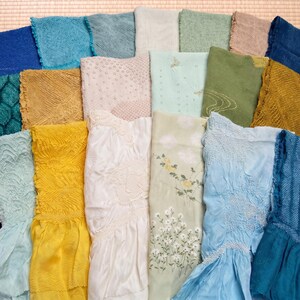 May include: A collection of colorful, textured fabrics in shades of blue, green, yellow, and white. Some fabrics feature intricate patterns and floral designs. The textiles are arranged on a woven mat, showcasing a variety of textures and hues.