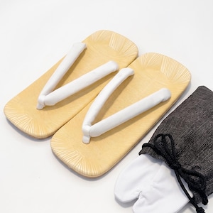 May include: A pair of traditional Japanese geta sandals with white thong straps, alongside a dark gray drawstring bag and white split-toe socks. The geta have a light wood color and are designed with a textured pattern.
