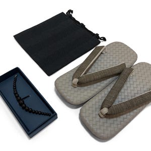 May include: An overhead shot shows a set of traditional Japanese geta sandals with a woven pattern, alongside a black drawstring bag and a dark blue jewelry box containing a black beaded necklace. The sandals are light gray with brown straps.